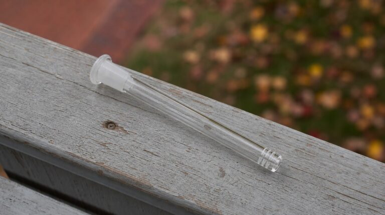 Wholesale smoking accessories: a clear 14mm glass downstem resting on a weathered porch rail.