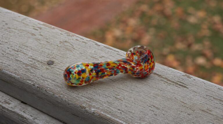 Speckled mixed-color glass hand pipe resting on a weathered porch rail, a wholesale pipes staple for smoke shop counters